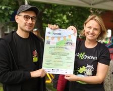 <p>Kobieta i mężczyzna trzymający plakat z zaproszeniem na piknik Ekosystemu</p>