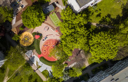 Na zdjęciu widoczne kolorowe podwórko z perspektywy drona. Jest zielono, widać między innymi plac zabaw i mini boisko do koszykówki. 