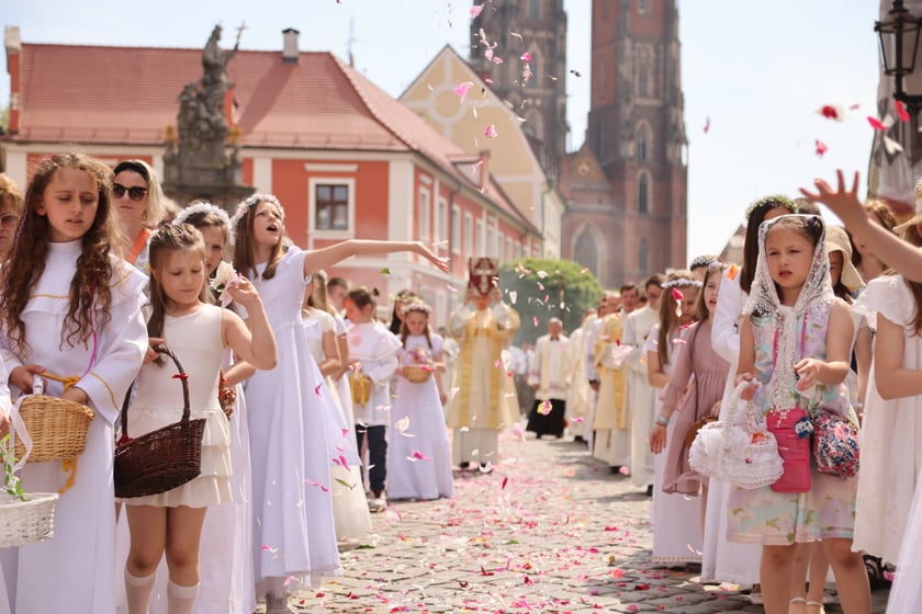 Procesja Bożego Ciała we Wrocławiu 2023. Dziewczynki w białych sukienkach i wiankach na głowie sypią płatki kwiatów. W tle katedra