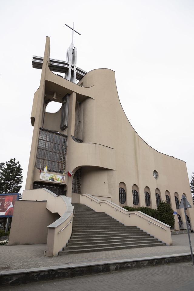 Kości&oacute;ł pw. Tr&oacute;jcy Świętej powstał na przebudowie budynku mieszkalnego. Starania o wzniesienie świątyni trwały kilkanaście lat. Projekt zrealizowano w latach 1979-1987. Bryła budowli jest zwarta, o zaokrąglonych narożach i tr&oacute;jkątnych aneksach. Dwie ściany zasłaniające dach wznoszą się łukami ku g&oacute;rze, tworząc w miejscu styku wieżę z przeszkleniem, spiętą konstrukcją żelbetową. W dolnej partii elewacji są arkadowe wnęki. W budowli mieści się kości&oacute;ł g&oacute;rny i dolny, zakrystia, pomieszczenia pomocnicze i księgarnia.