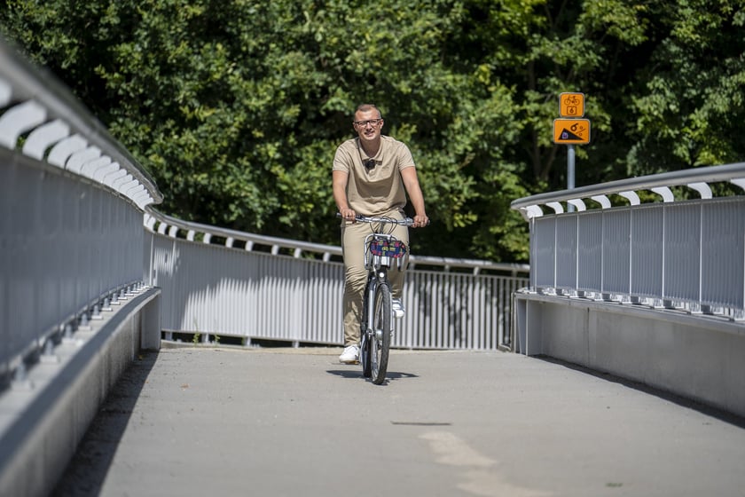 Mateusz Żak, wiceprezydent Wrocławia jedzie rowerem przez kładkę nad Widawą.