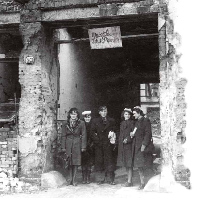 Grupa studentów przy zrujnowanej bramie z napisem Wyższa Szkoła Sztuk Plastycznych  na ul. R. Traugutta (1946)