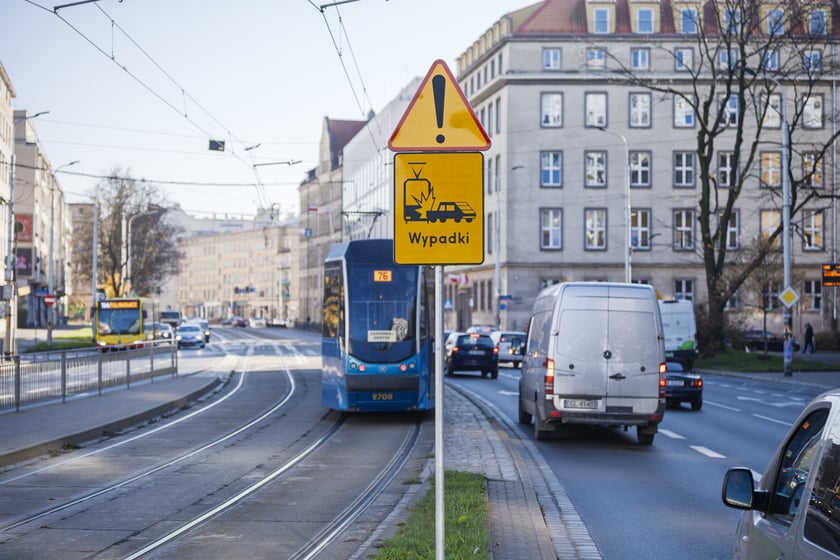 Ulica z torowiskiem i jezdnią oraz widocznym znakiem ostrzegawczym z tablicą zawierającą piktogram kolizji tramwaju z samochodem i napis "Wypadki".  Tablica ostrzegająca o niebezpiecznym miejscu na pl. Legionów.