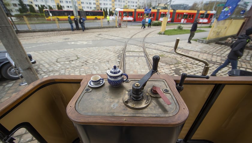 Stanowisko motorniczego w przedwojennym tramwaju. Nad nim pantograf, w ręku wajcha, przed nim piękne miasto i szyny.