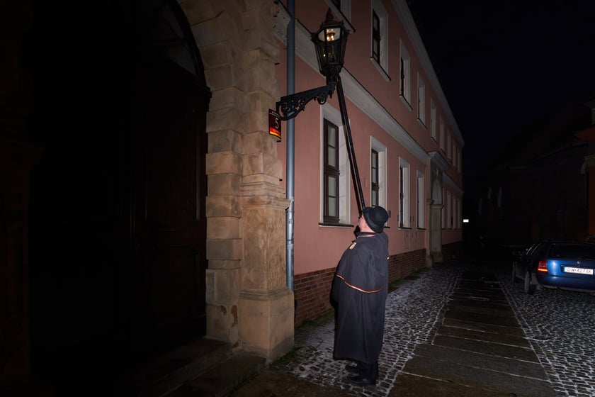 Na zdjęciu widać mężczyznę, który zapala latarnię na Ostrowie Tumskim we Wrocławiu