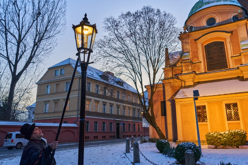 Na zdjęciu widać mężczyznę, który zapala latarnię na Ostrowie Tumskim we Wrocławiu