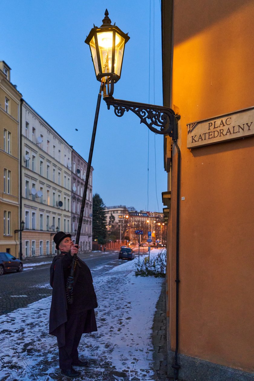 Na zdjęciu widać mężczyznę, który zapala latarnię na Ostrowie Tumskim we Wrocławiu