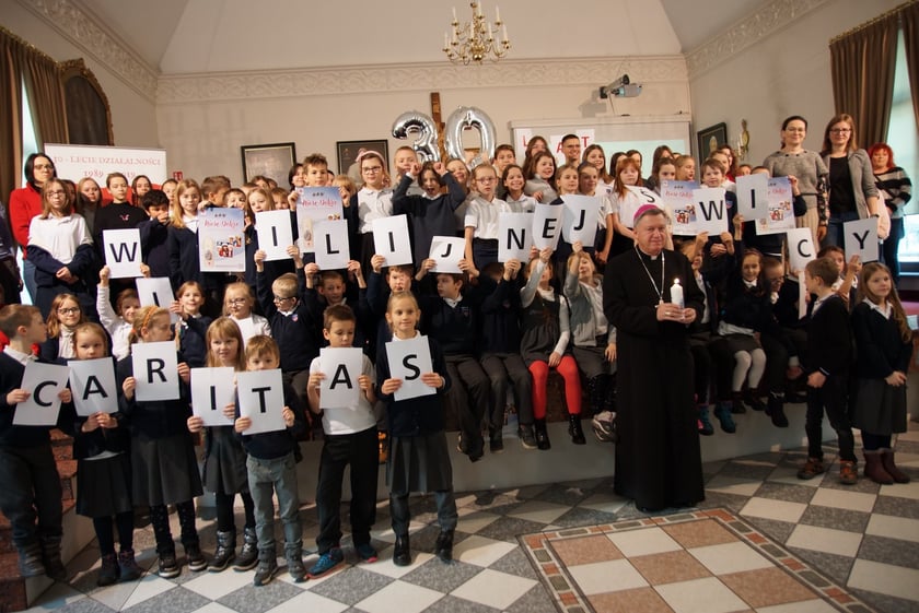 Dzieci trzymające karteczki z literami mającymi układać się w napis związany ze świecami wigilijnymi Caritas