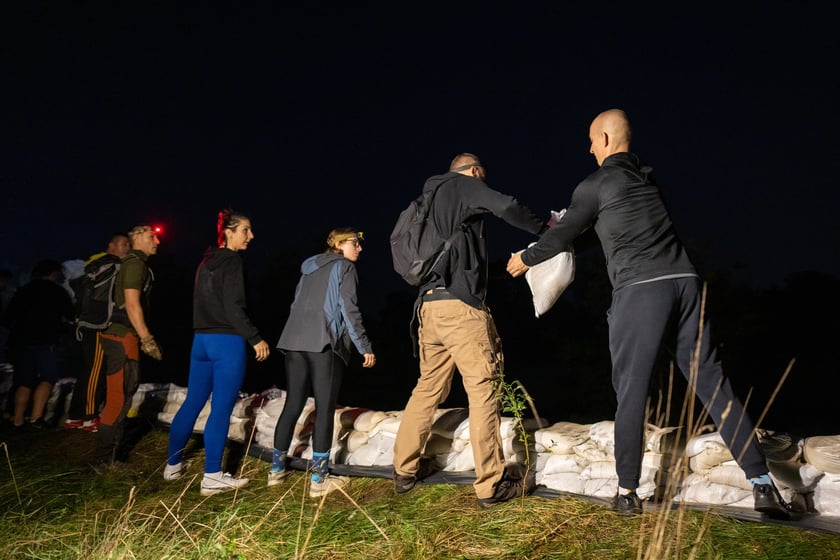 Kobiety i mężczyźni układają worki z piaskiem na Marszowicach w nocy z 17 na 18 września 2024 roku