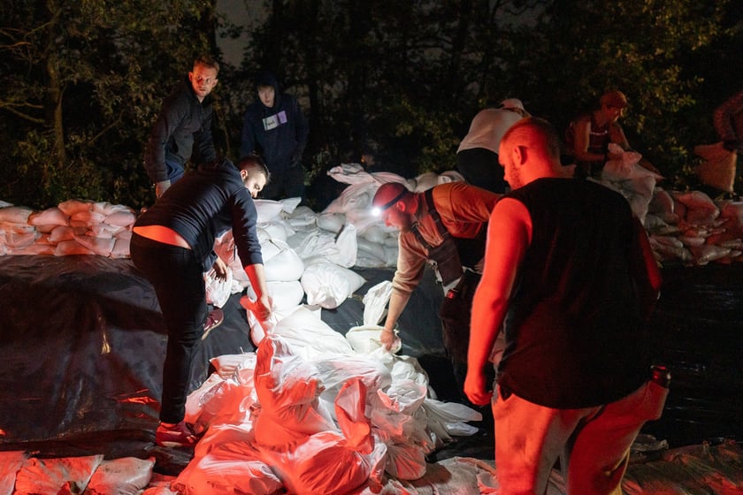 Kobiety i mężczyźni układają worki z piaskiem na Marszowicach w nocy z 17 na 18 września 2024 roku