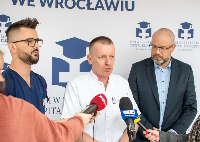 Na zdjeciu trzech mężczyzn przed mikrofonami różnych stacji radiowych i telewizyjnych. Od lewej: Andrzej Mędrala, ratownik i pielęgniarz koordynujący w SOR USK we Wrocławiu, dr Janusz Sokołowski, kierownik Szpitalnego Oddziału Ratunkowego USK, lek. Maciej Kamiński, wicedyrektor ds. medycznych USK we Wrocławiu