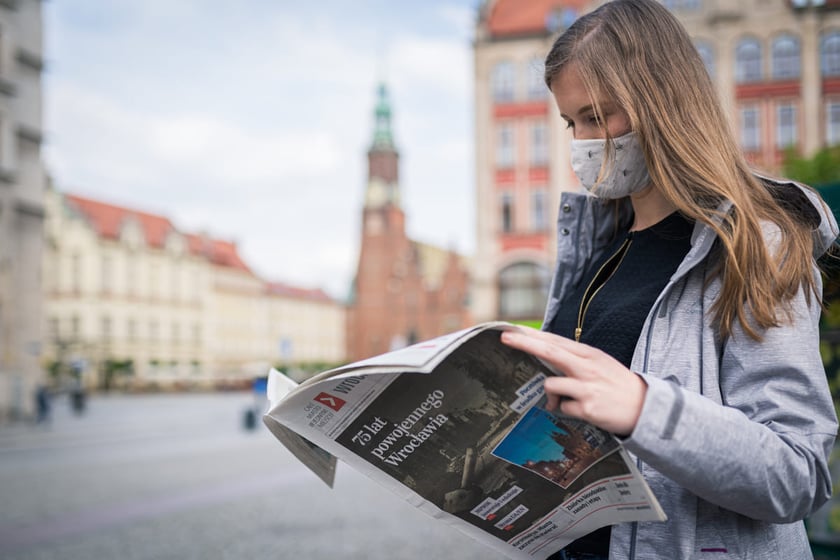 Kobieta w maseczce czytająca biuletyn, w tle wrocławski ratusz.