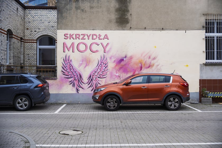 Różowe skrzydła z napisem SKRZYDŁA MOCY namalowane na ścianie szpitala na Hirszfelda