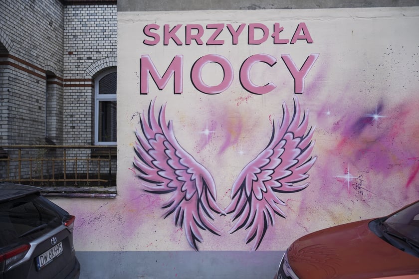 Różowe skrzydła z napisem SKRZYDŁA MOCY namalowane na ścianie szpitala na Hirszfelda