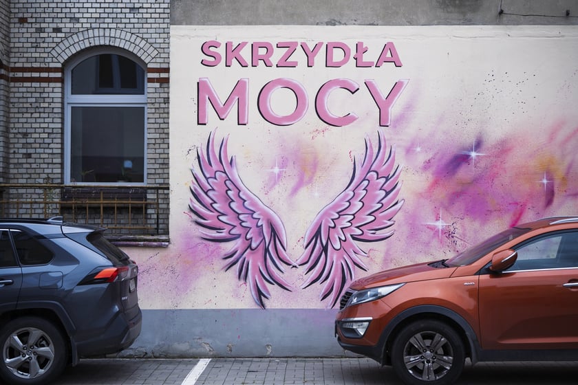 Różowe skrzydła z napisem SKRZYDŁA MOCY namalowane na ścianie szpitala na Hirszfelda