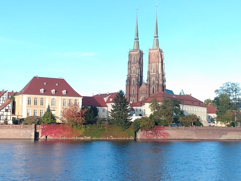 Na zdjęciu ceglane mury przeciwpowodziowe nad Odrą porośnięte zmieniającym kolor z zielonego na czerwony winobluszczem. W tle widok Na Ostrów Tumski i katedrę .