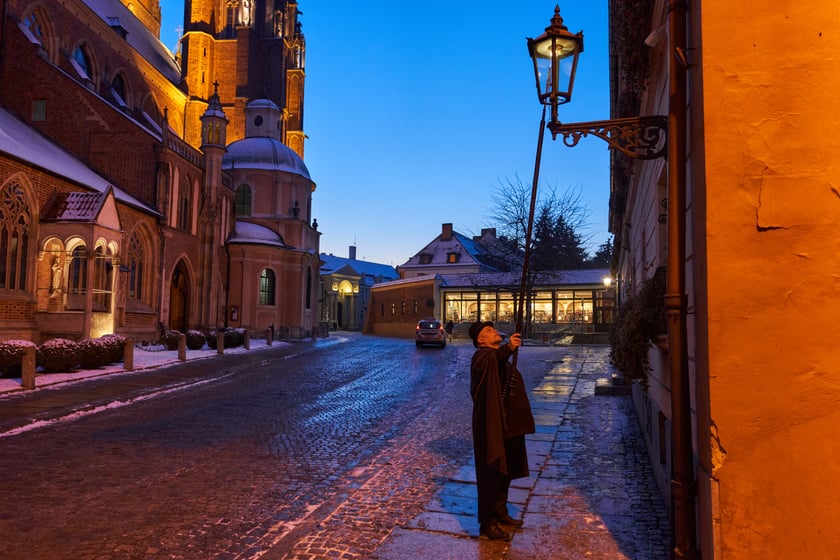 Na zdjęciu widać mężczyznę, który zapala latarnię na Ostrowie Tumskim we Wrocławiu