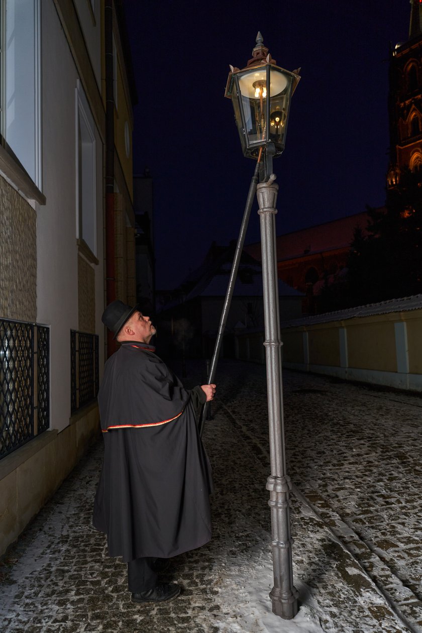 Na zdjęciu widać mężczyznę, który zapala latarnię na Ostrowie Tumskim we Wrocławiu