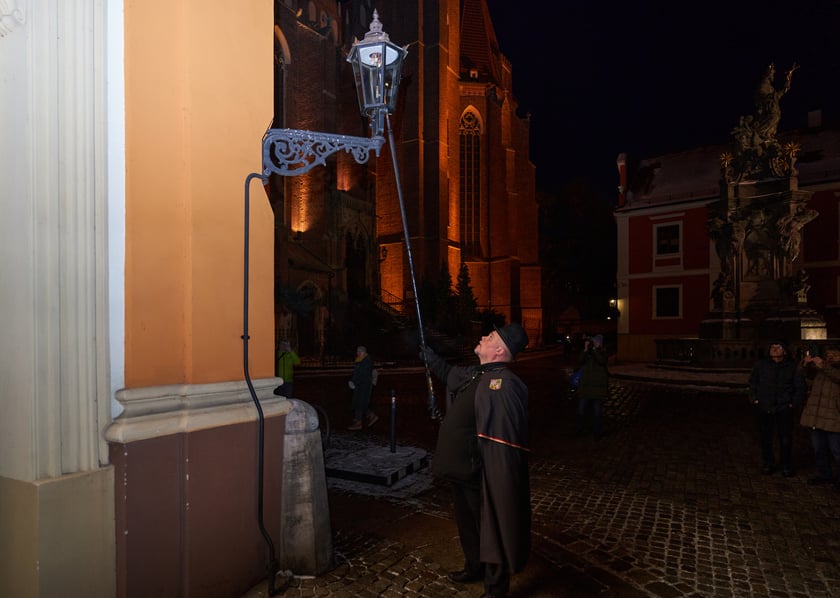 Na zdjęciu widać mężczyznę, który zapala latarnię na Ostrowie Tumskim we Wrocławiu