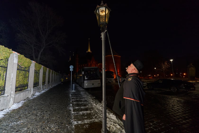 Na zdjęciu widać mężczyznę, który zapala latarnię na Ostrowie Tumskim we Wrocławiu