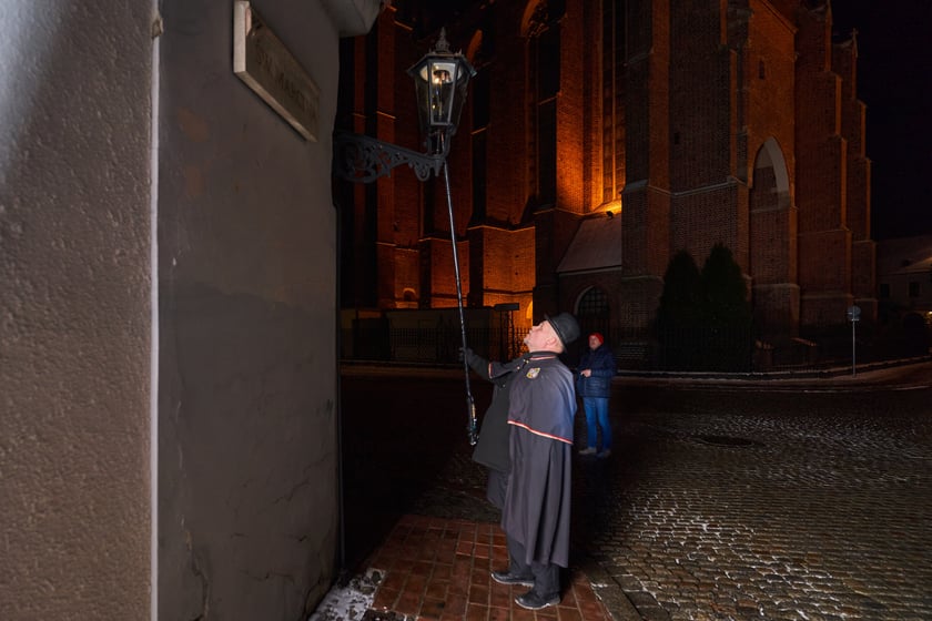 Na zdjęciu widać mężczyznę, który zapala latarnię na Ostrowie Tumskim we Wrocławiu