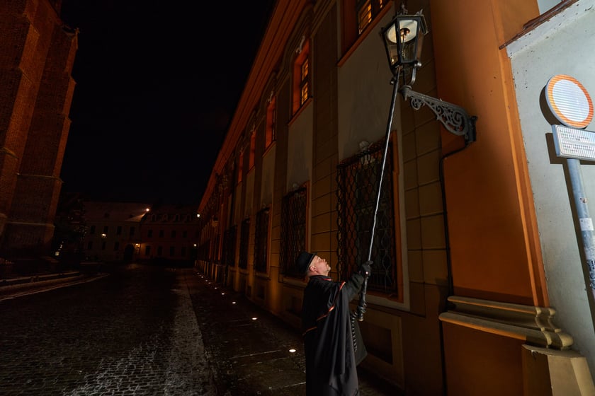 Na zdjęciu widać mężczyznę, który zapala latarnię na Ostrowie Tumskim we Wrocławiu