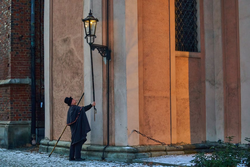 Na zdjęciu widać mężczyznę, który zapala latarnię na Ostrowie Tumskim we Wrocławiu