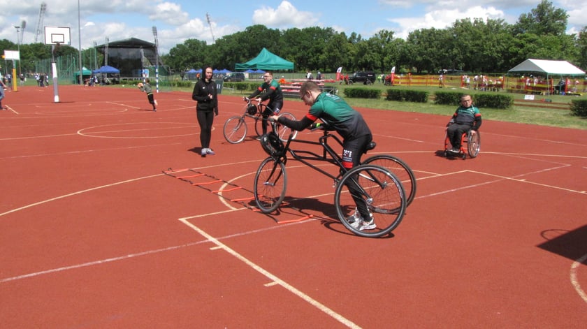 Pokaz frame runningu, dyscypliny sportowej dla os&oacute;b z niepełnosprawnościami. Mężczyzna biegnie, opierając się na tr&oacute;jkołowym rowerze