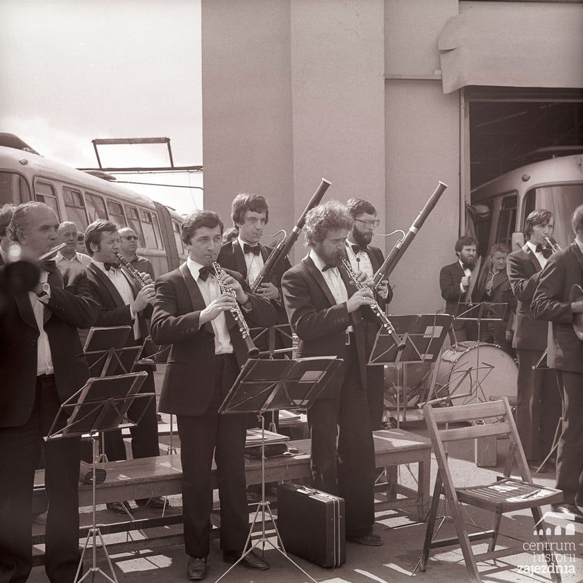 Na zdjęciu widoczna część orkiestry Opery Wrocławskiej (instrumenty dęte) przed halą zajezdni autobusowej nr VII. Widoczni m.in. Zbigniew Marynowski, Roman Astriab, Stefan Małek, Roman Augustyn, Ryszard Rybczyński.
