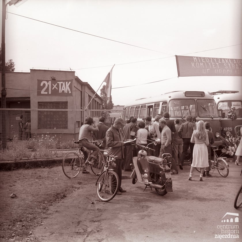 Na zdjęciu brama wjazdowa do zajezdni autobusowej nr VII, dwa autobusy jelcz 043, transparent „21 x tak” i transparent Międzyzakładowego Komitetu Strajkowego.