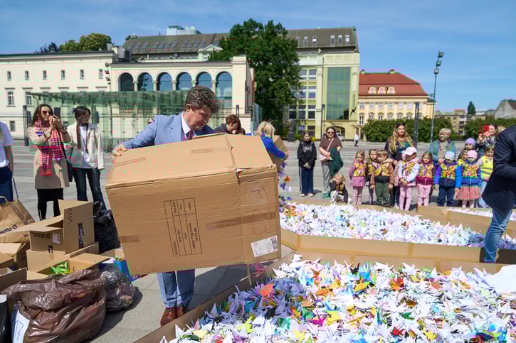 Wiceprezydent Ryszard Kessler dosypuje papierowych żurawi do napisu