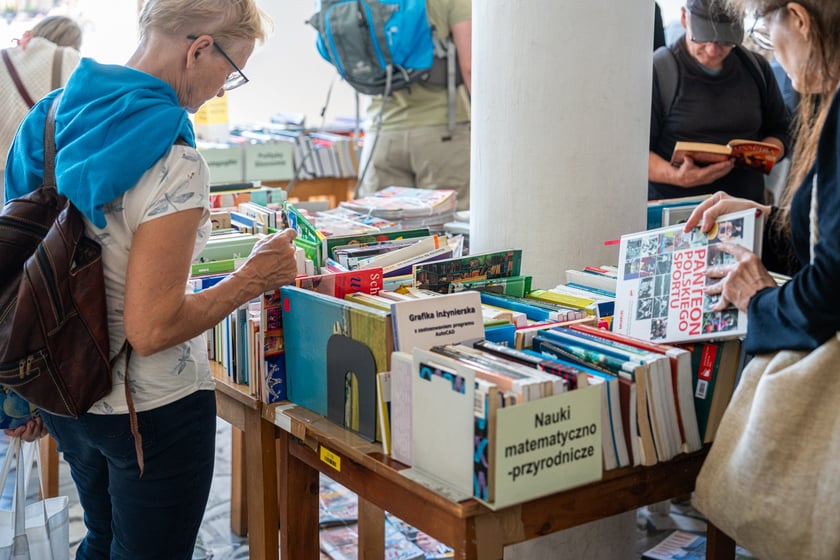 Czytelnicy przeglądający książki i inne zbiory wystawione na sprzedaż w Dolnośląskiej Bibliotece Publicznej w rynku