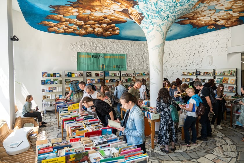 Czytelnicy przeglądający książki i inne zbiory wystawione na sprzedaż w Dolnośląskiej Bibliotece Publicznej w rynku