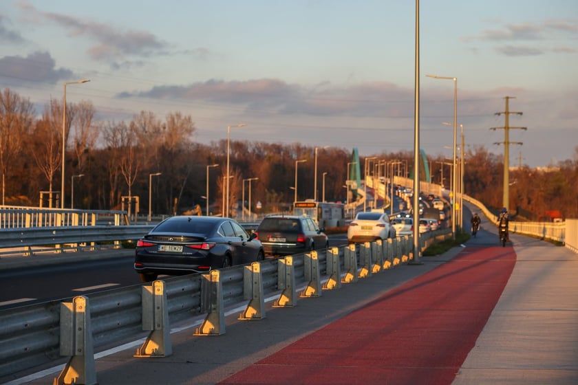 Aleja Wielkiej Wyspy w blasku zachodzącego słońca. Droga rowerowa i oddzielona od niej ulica z samochodami