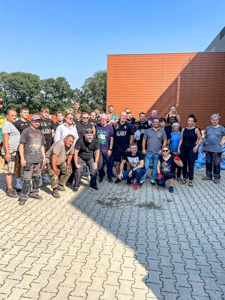 Piłkarze ręczni Śląska (ubrani w klubowe stroje) nasypują łopatami piach do worków i wrzucają je na naczepę