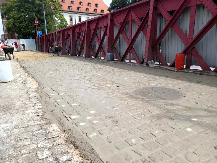 Kostka na moście jest już zaspoinowana. Trwa piaskowanie.