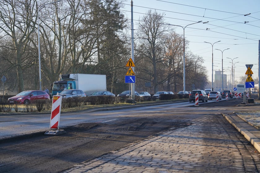Powiększ obraz: Jezdnia ze sfrezowanym asfaltem na jednym pasie i auta jadące po drugim - remontowany fragment ul. Powstańców Śląskich.