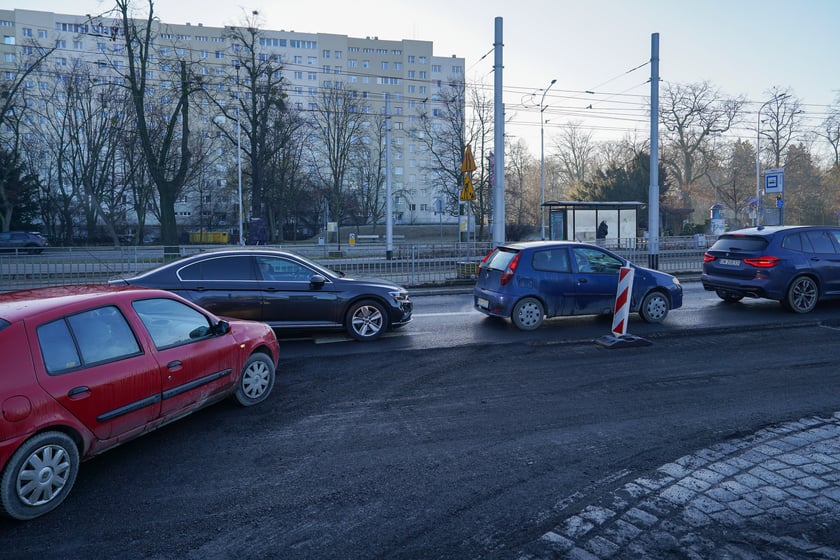 Powiększ obraz: Jezdnia ze sfrezowanym asfaltem na jednym pasie i auta jadące po drugim - remontowany fragment ul. Powstańców Śląskich.