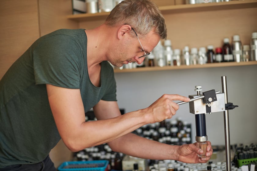 Karol Jaśkowiak butelkuje perfumy używając specjalnej maszyny