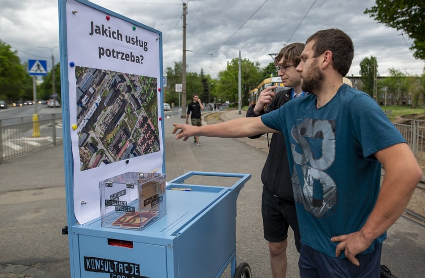 Konsultacje w sprawie terenu TBS-u przy ul. Głubczyckiej we Wrocławiu. Na zdjęciu widać dwóch mężczyzn analizujących plan inwestycji zawieszony na wózku konsultacyjnym.