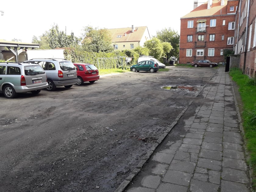 Podwórko przy Hallera przed rewitalizacją - widok na nieutwardzony parking z dziurami i kałużami