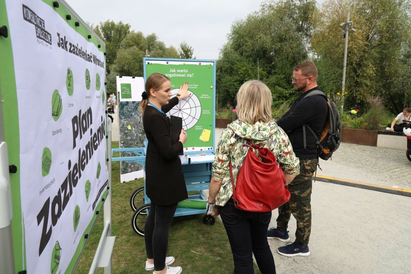 Trójka ludzi stoi w parku obok wózka konsultacyjnego i rozmawia.