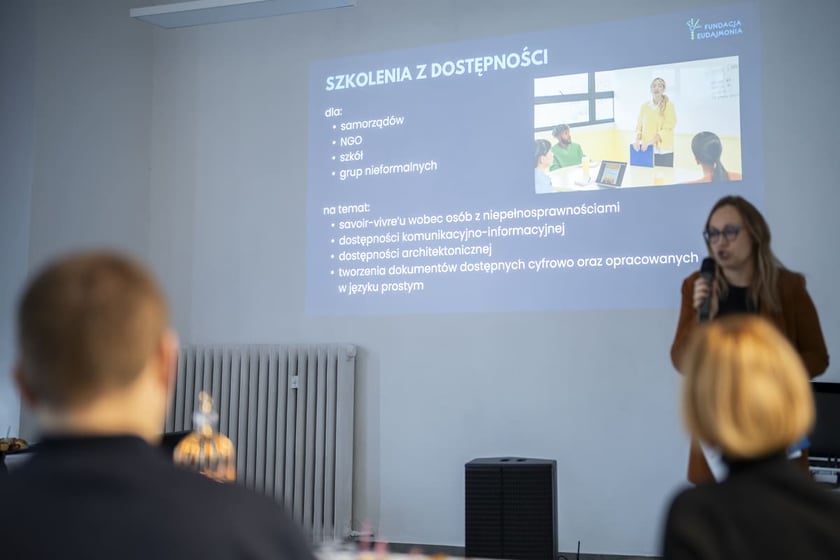 Otwarcie Centrum Edukacyjno-Treningowego przy placu Legion&oacute;w 1-2. Wrocław, 15.01.2025. W tle slajd prezentacji o szkoleniach z dostępności, przy mikrofonie Joanna Burkiewicz