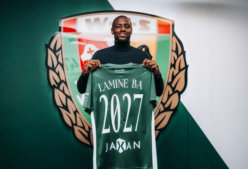 Powiększ obraz: Zawodnik stojący na tle klubowego herbu z koszulką sportową -  Lamine Ba - nowy obrońca Śląska Wrocław.