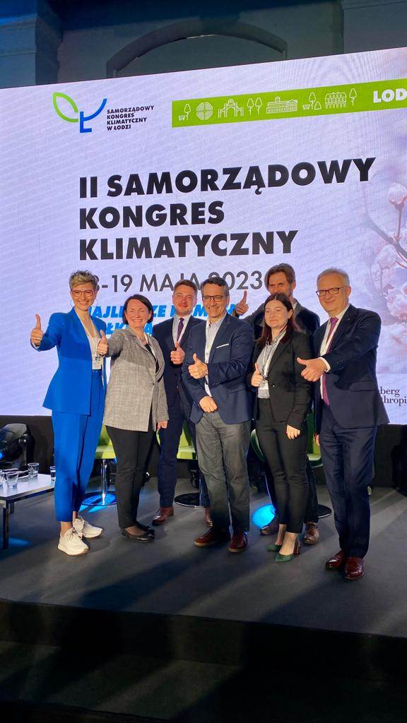 Uczestniczący II Samorządowego Kongresu Klimatycznego w Łodzi przed banerem z napisem II Samorządowy Kongres Klimatyczny 18-19 maja 2023