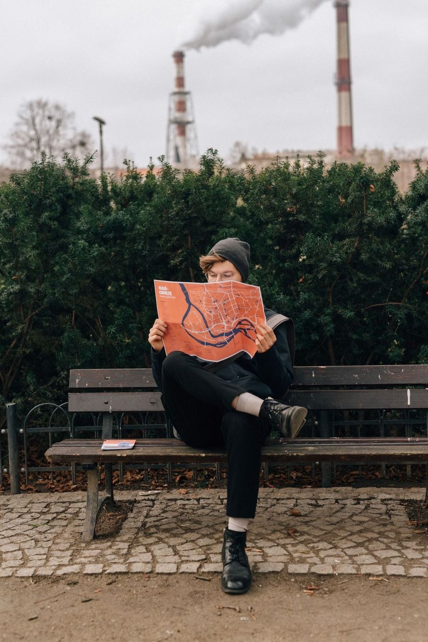 <p>Młody człowiek siedzący na ławce z mapą osiedla stworzoną w ramach Mikrogrant&oacute;w. Zdjęcie archiwalne.</p>