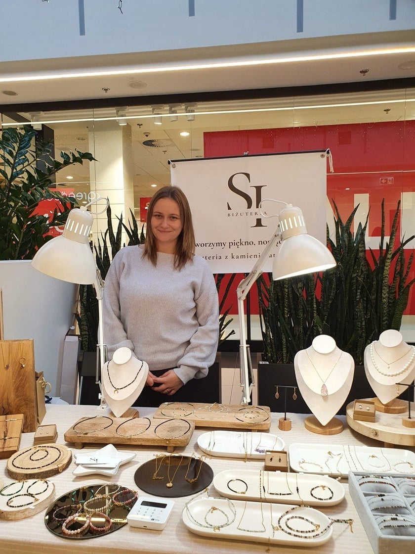<p>Na zdjęciu kobieta na stoisku z autorską biżuterią</p>