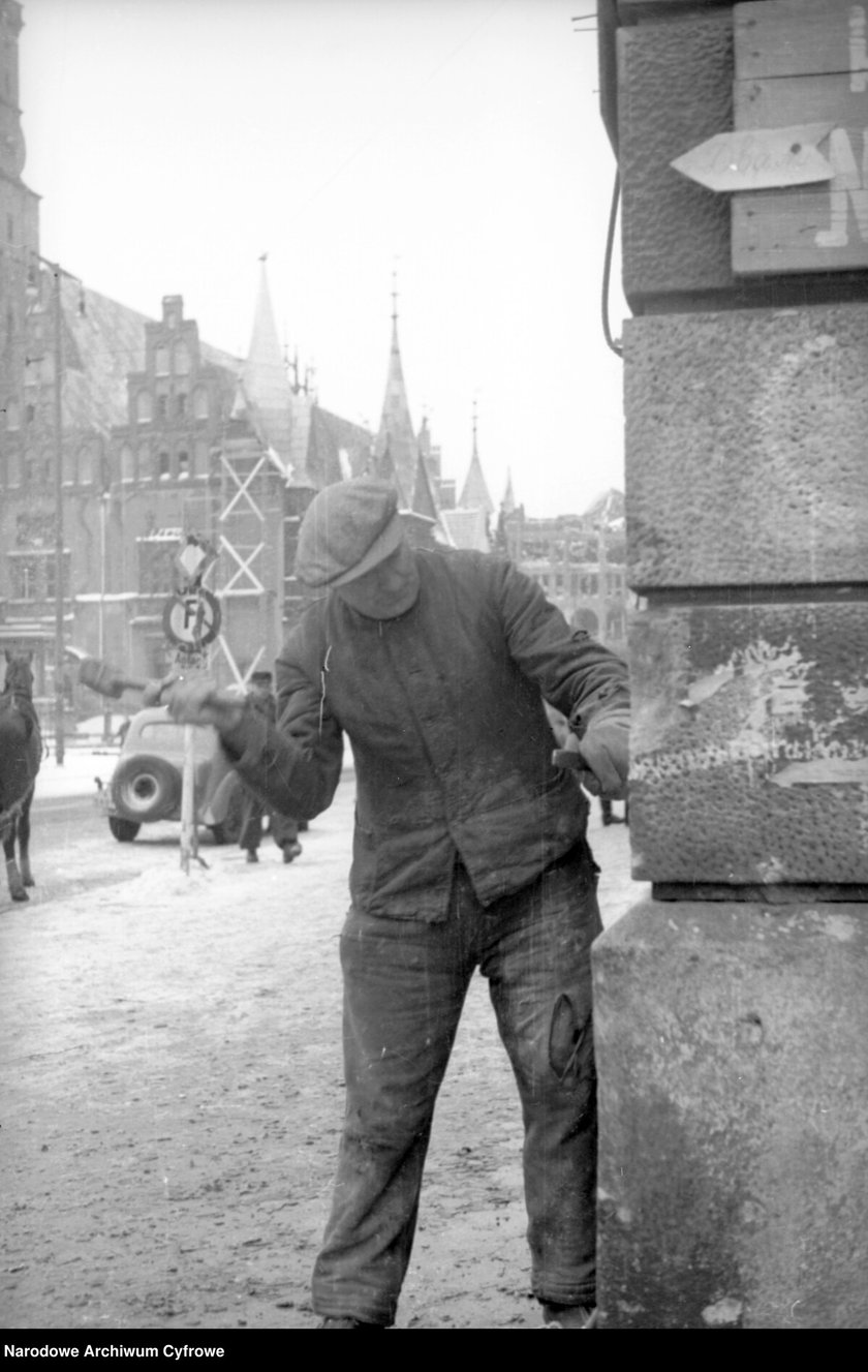 Powiększ obraz: <p>Rynek, lata 1945 - 1946, robotnik skuwający niemieckie napisy z elewacji kamienicy</p>