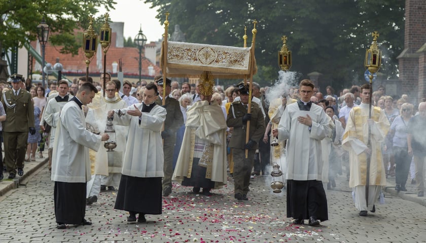 Procesja z okazji Bożego Ciała we Wrocławiu. Zdjęcie archiwalne. Na zdjęciu ksiądz niesie monstrancje pod baldachimem, wokół idą duchowni i wierni