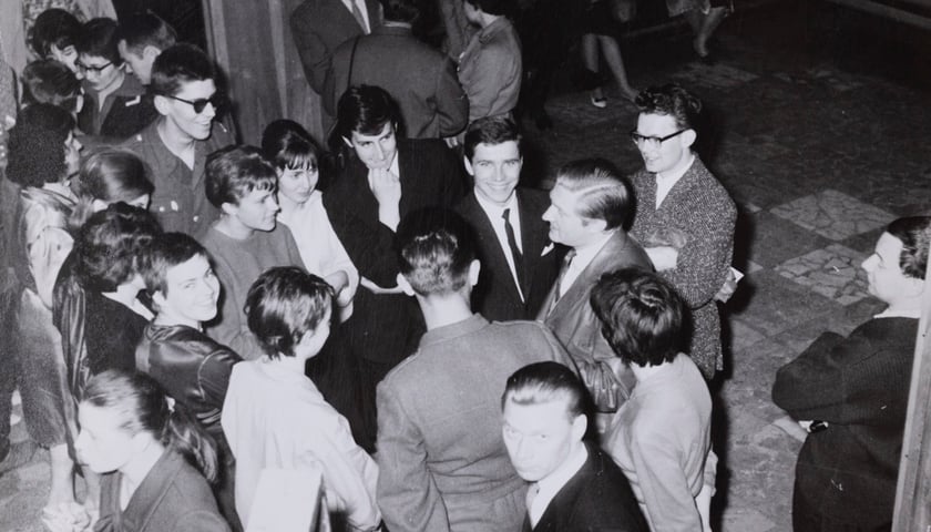 Na zdjęciu z lata 60. grupa młodych osób elegancko ubranych stoi wokół mężczyzny w średnim wieku. Aktor Igor Przegrodzki z uczestnikami konkursu recytatorskiego